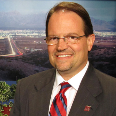 Portrait of a professional man in a suit and tie, smiling in front of a scenic background.