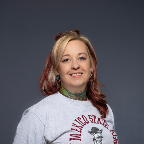 Portrait of a woman with colorful hair, wearing a New Mexico State Aggies t-shirt.