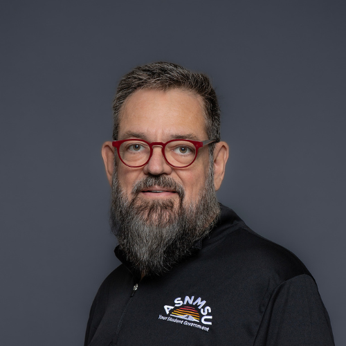 Headshot of a man with a beard and glasses, wearing a black ASNMU polo shirt.